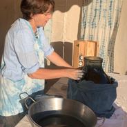 Artisane avec talier bleu et blanc en train de teindre dans une marie-jeanne en verre.