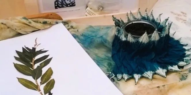 Herbier et textile Plan serré d'une planté séchée sur l'herbier de gauche et tissus bleu foncé froncé autour d'un petit bocal.